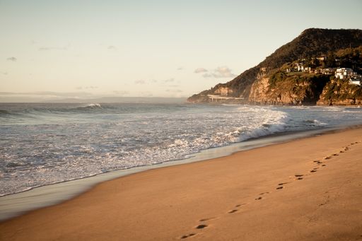 A sea from the beach surrounded by hills covered in forests and buildings under sunlight