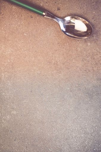 A vertical shot of a shiny metal spoon on a rough stone surface with space for your text