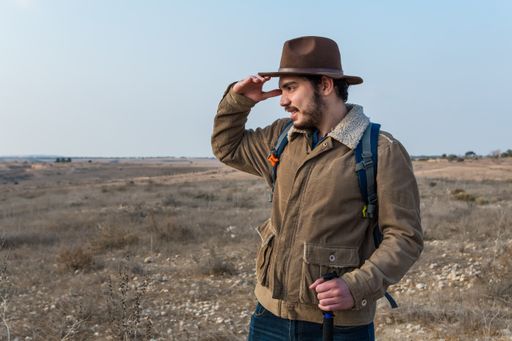 A view of a Caucasia hiker man with a beard, wearing a brown jacket, backpack and a cowboy hat