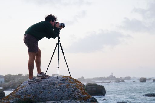 A young photographer taking a picture of the sea while standing on the rock in Brignogan, France
