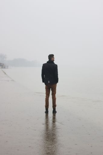 A cool man standing on the side of a river while raining