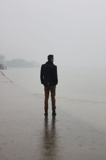 A vertical shot of a guy standing on the bay of a river on a rainy day