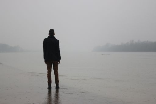 A man standing on the side of a river while raining