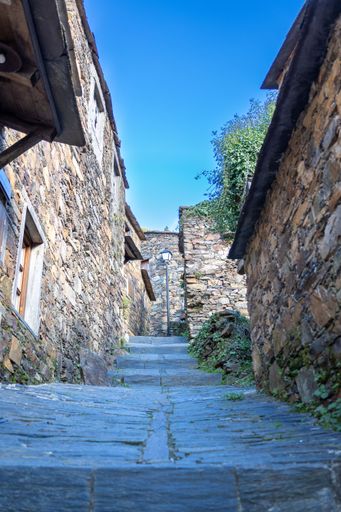 A vertical shot of an ancient schist stone alley surrounded by mossy houses in a village in Portugal