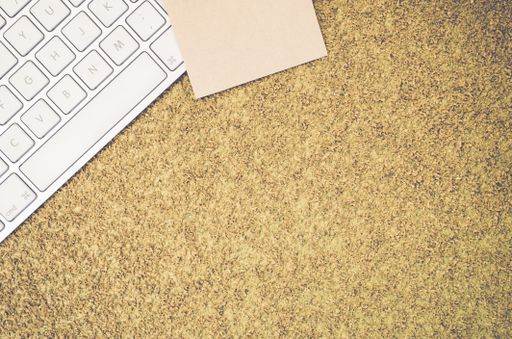 A top view of a computer keyboard on an office desk and a blank sticky note with copy space