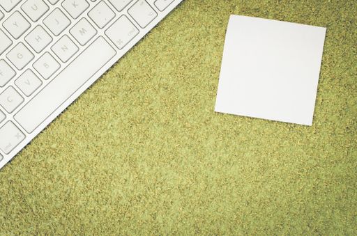 A top view of a computer keyboard on an office desk and a blank sticky note with copy space