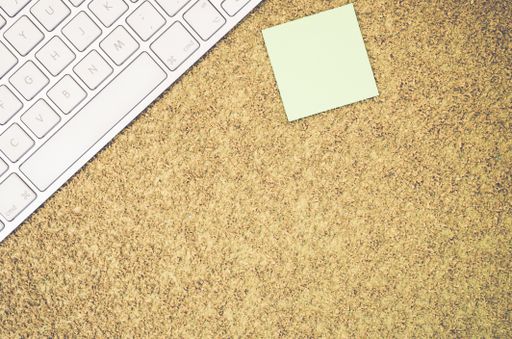 A top view of a computer keyboard on an office desk and a blank sticky note with copy space