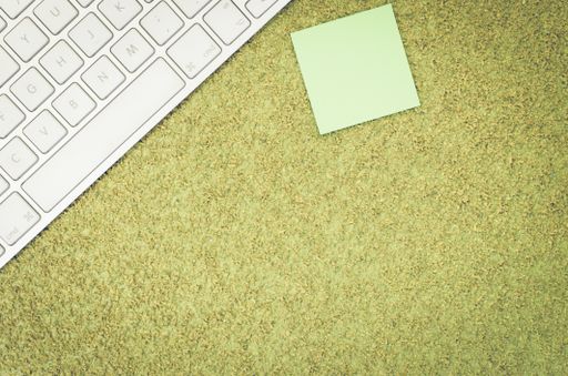 A top view of a computer keyboard on an office desk and a blank sticky note with copy space