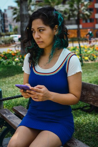 A vertical shot of a Caucasian woman with blue hair chatting with her phone in the park
