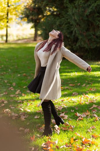 A vertical shot of a beautiful Caucasian girl wearing a coat and having fun in a park during daylight