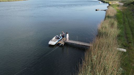 Two people standing on the wooden pier and looking at the boat on the lakeside