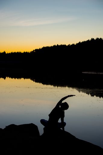A vertical shot of a silhouette of a young female doing yoga with a beautiful sunrise in front of her