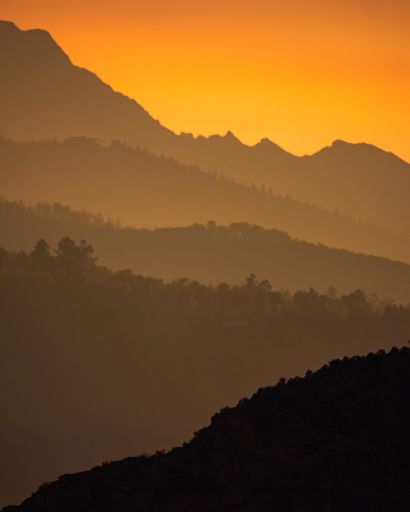A vertical shot of layers of forested mountains at sunset