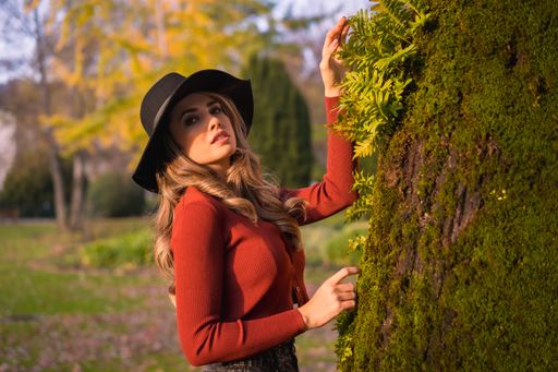 A blonde Caucasian woman wearing a hat posing in the park near the tree covered with moss