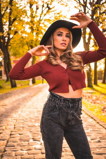 A vertical shot of a blonde Caucasian attractive woman wearing a hat posing in the park with the sun shining