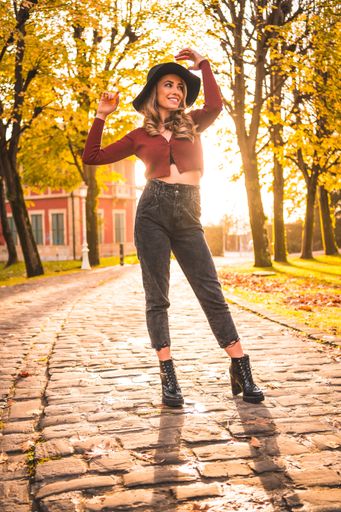 A vertical shot of a blonde Caucasian attractive woman wearing a hat posing in the park with