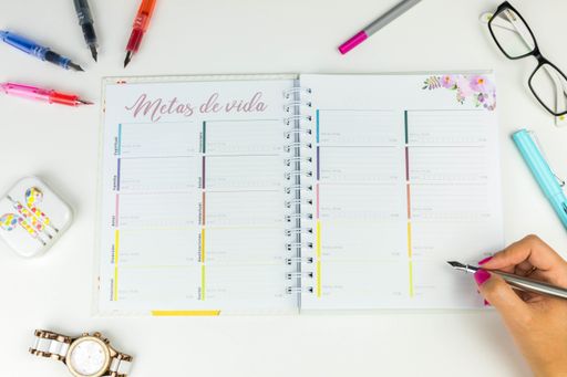 A top view closeup of a colorfully organized journal next to a watch, headphones, glasses on the table