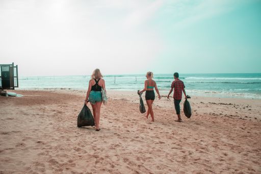 Two girls and a guy walking on the beach carrying black garbage bags