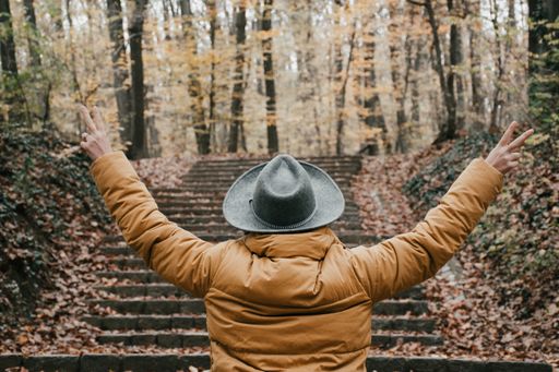 A woman in the woods during autumn making a peace hand sign with her back to the camera