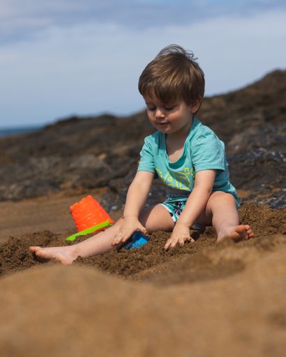 A shallow focus of an adorable little boy playing with his toys on the sandy beach
