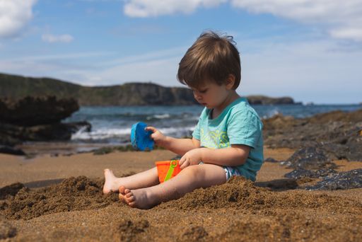 A shallow focus of an adorable little boy playing with his toys on the sandy beach