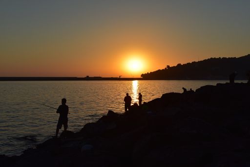 The silhouettes of people fishing surrounded by the sea under the sunlight during a golden sunset