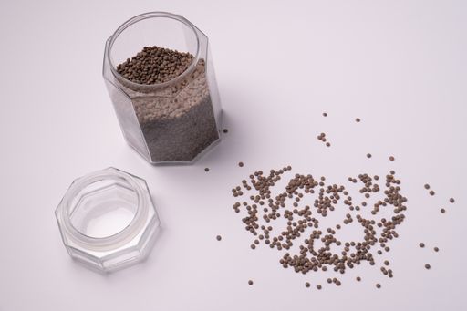 A high angle shot of brown lentils scattered on a white surface and filled in a glass jar