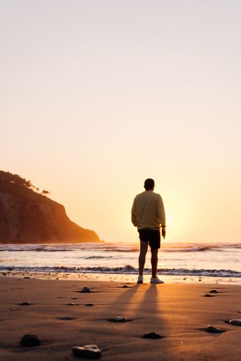 A lonely person walking on a beach at sunset