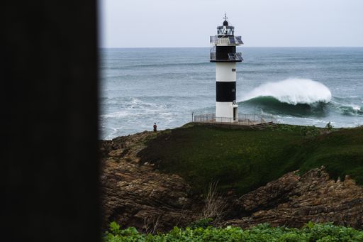 A tall lighthouse by the sea with splashing waves in the background