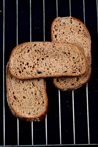 A top view closeup of a sliced loaf of brown bread on metal wires on a dark background