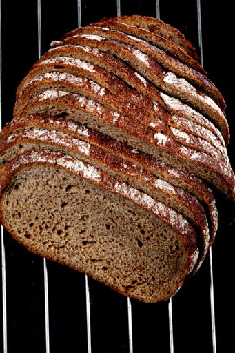 A top view closeup of a sliced loaf of brown bread on metal wires on a dark background