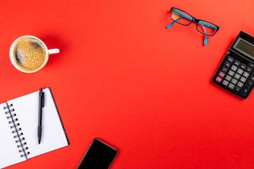 A flat lay of office supplies and a cup of coffee on a red surface with space for your text - office work concept