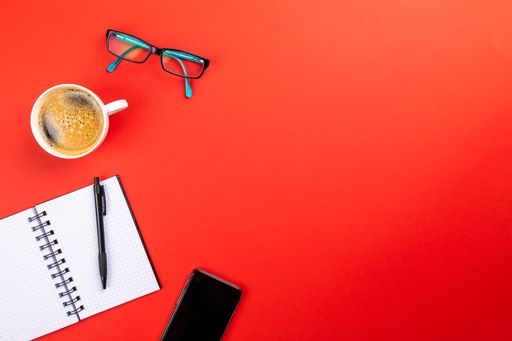 A flat lay of office supplies and a cup of coffee on a red surface with space for your text - office work concept
