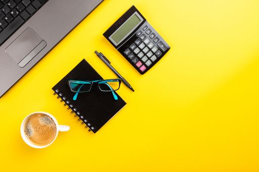 A flat lay of office supplies and a cup of coffee on a yellow surface with space for your text - office work concept