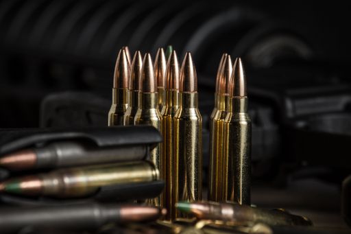 Various 223 rifle bullets standing or laying next to a full AR-15 magazine full of ammo