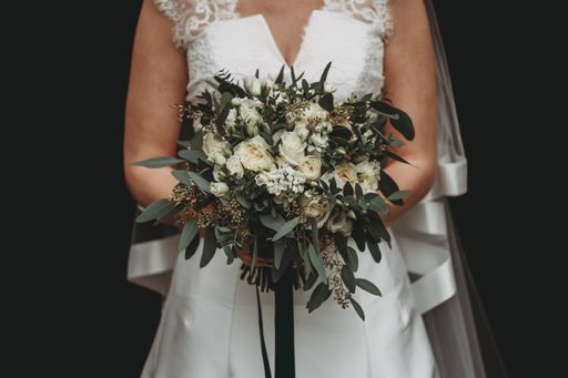A bride with a white wedding dress holding a beautiful flower bouquet against a black background