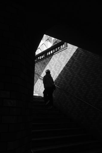 A grayscale shot of a person climbing up the underground stairs under the sunlight