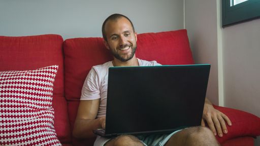 A young caucasian male sitting on a couch while working on his laptop from home