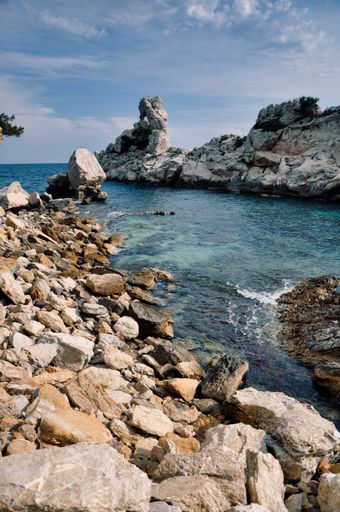 A vertical shot of a rocky coast on a sea under the blue sky