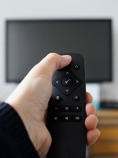 A hand holding a remote control for turning the TV on han