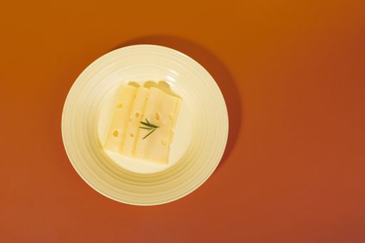 A top view of Swiss cheese slices with rosemary on a plate isolated on an orange background