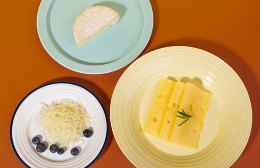 A top view of camembert, Swiss cheese, and grated cheese with blueberries and rosemary on plates