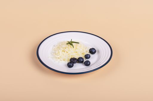 A closeup of grated cheese with rosemary and blueberries on a plate isolated on a light brown background