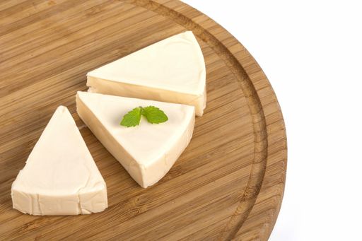 A high angle shot of triangle cream cheese pieces with mint on a wooden board isolated on a white background