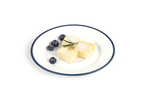 A closeup of parmesan cheese pieces with blueberries and rosemary on a plate against a white background