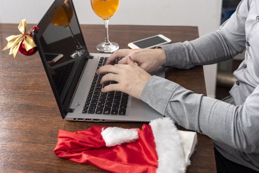 A closeup of a Hispanic man working on his computer with a Santa hat next to it on a wooden table