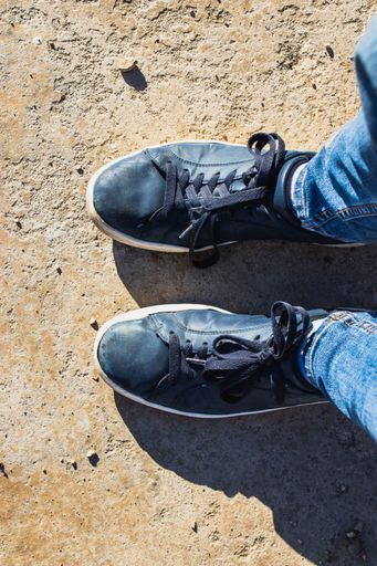 A top view of a person wearing blue leather sneakers and jeans outdoors