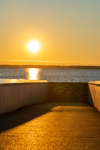 A vertical view of a pier at the sea with the bright sun shining on horizon during sunset