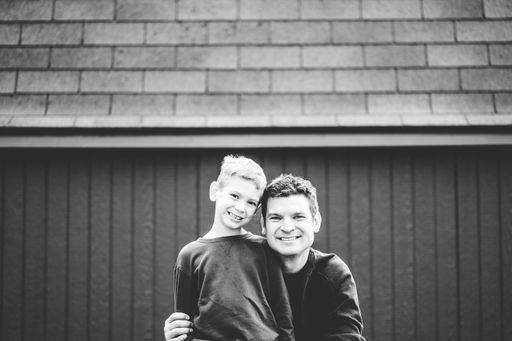 A greyscale shot of a father and his son posing in front of their house