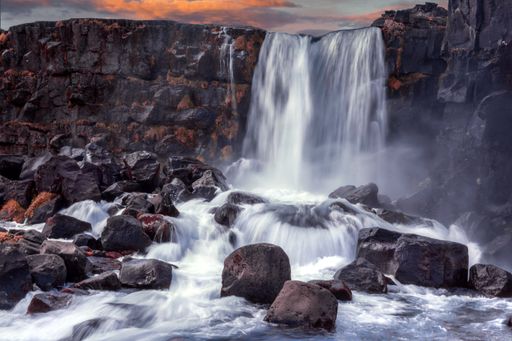 A scenic view of the Oxararfoss waterfall flowing over the rocks at sunset, Thingvellir